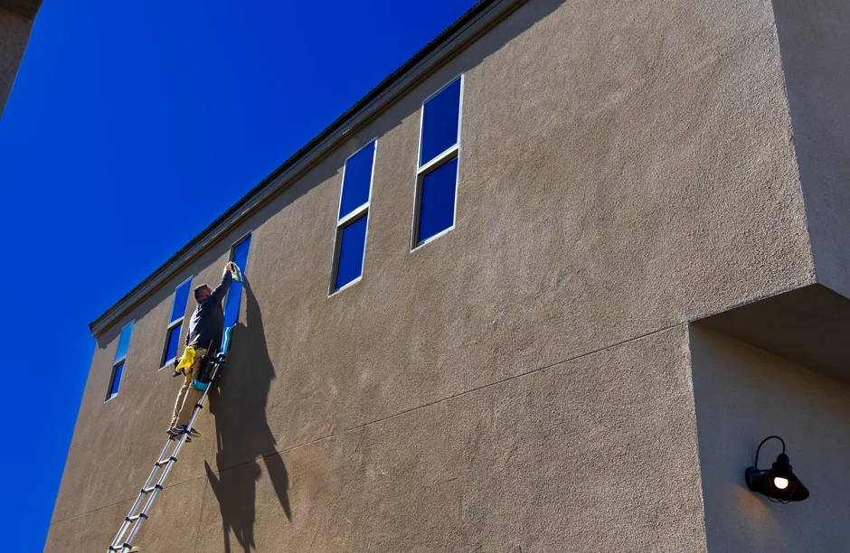 Three window cleaners suspended on ropes clean a modern glass building facade during the day.